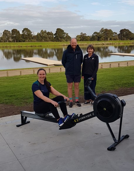 Competitor Francine Dudfield sitting on a rowing erg with Toorak College rowing staff