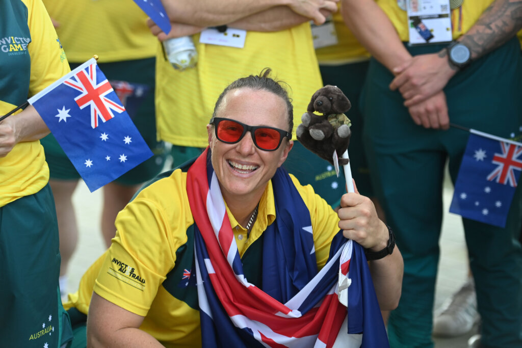 Invictus Alumni Taryn Dickens smiles with an Australian flag and Invictus Games mini mascot